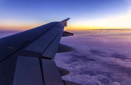 View of airplane wing above the clouds at sunrise, symbolising premium flight deals with a business class travel consolidator